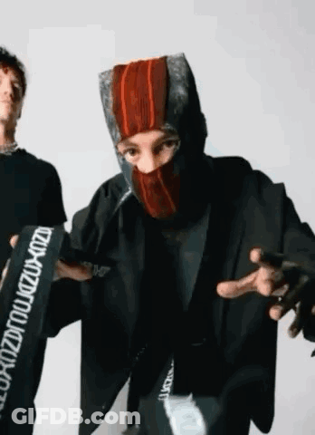 A Man Wearing A Mask Is Standing Next To Another Man Wearing A Jacket . GIF