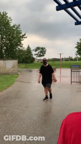 A Man Wearing A Mask Is Walking Down A Wet Street . GIF