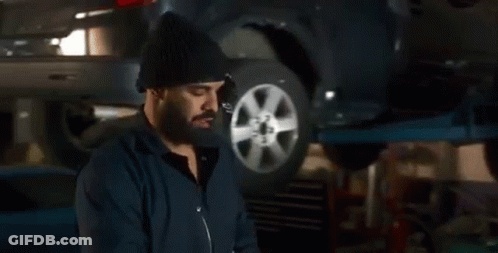 A Man Wearing A Mask Is Working On A Car On A Lift In A Garage . GIF