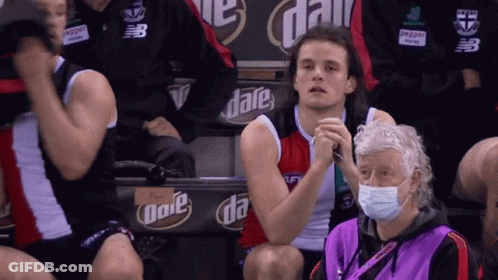 A Man Wearing A Mask Sits In A Stadium With A Sign That Says Date On It GIF