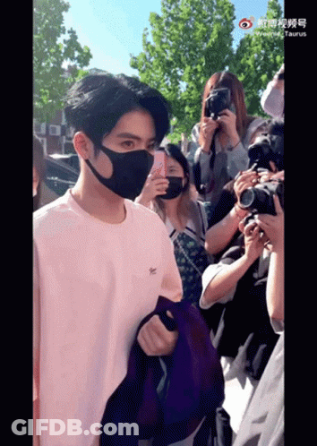 A Man Wearing A Mask Stands In Front Of A Crowd GIF