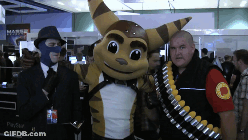 A Man Wearing A Mask Stands Next To A Raccoon Mascot And A Playstation Bag GIF