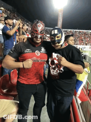 A Man Wearing A Mask Stands Next To Another Man Wearing A Shirt That Says ' Nissan ' On It GIF