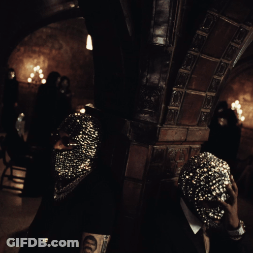 A Man Wearing A Mask With Rhinestones Is Standing In A Dark Room GIF