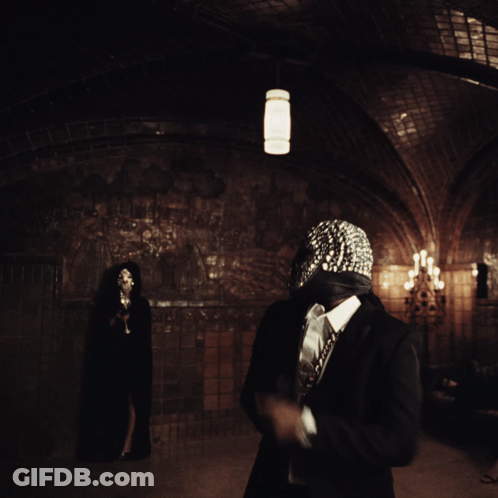 A Man Wearing A Mask With Rhinestones Is Standing In A Dark Room GIF