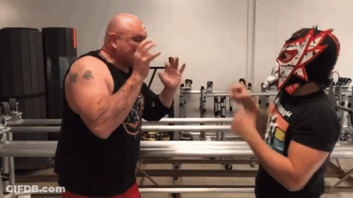 A Man Wearing A Mask With The Letter N On It Stands Next To A Bald Man GIF