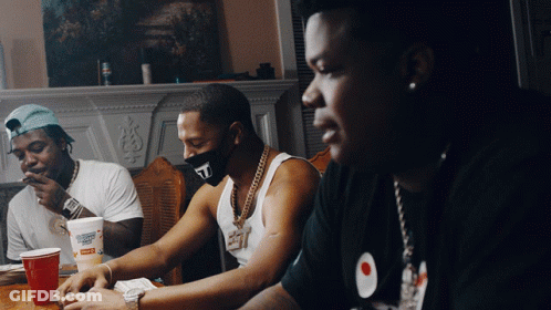 A Man Wearing A Mask With The Letter T On It Sits At A Table With Other Men GIF