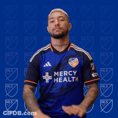 A Man Wearing A Mercy Health Jersey Stands In Front Of A Blue Background GIF