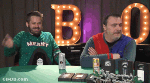 A Man Wearing A Merry Sweater Is Sitting At A Table GIF