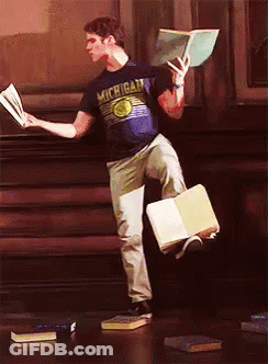 A Man Wearing A Michigan Shirt Is Holding A Book In His Hand GIF