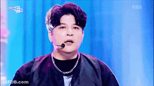 A Man Wearing A Microphone And A Necklace On A Stage With Kbs Written On The Bottom Of The Screen GIF