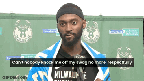 A Man Wearing A Milwaukee Bucks Shirt Is Standing In Front Of A Green Backdrop GIF