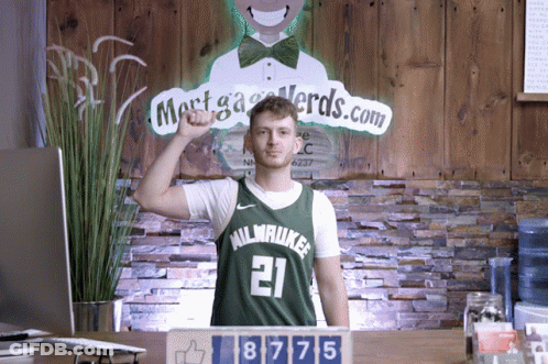 A Man Wearing A Milwaukee Jersey Stands In Front Of A Sign That Says Mortga Nerds.com GIF
