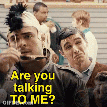 A Man Wearing A Mohawk Hat Is Talking To Another Man Who Is Holding A Stuffed Animal . GIF