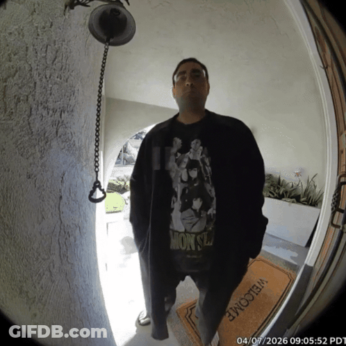A Man Wearing A Monsters Shirt Stands In Front Of A Door GIF
