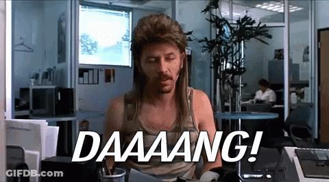 A Man Wearing A Mullet Is Sitting At A Desk And Says Daaaang ! GIF