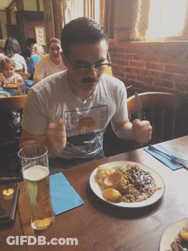 A Man Wearing A Mustache Is Sitting At A Table With A Plate Of Food GIF