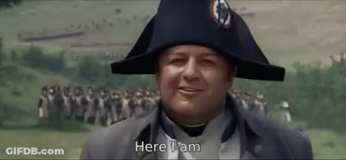 A Man Wearing A Napoleon Hat Is Standing In Front Of A Crowd And Says Here I Am . GIF