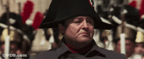 A Man Wearing A Napoleon Hat Stands In Front Of A Crowd Of People GIF