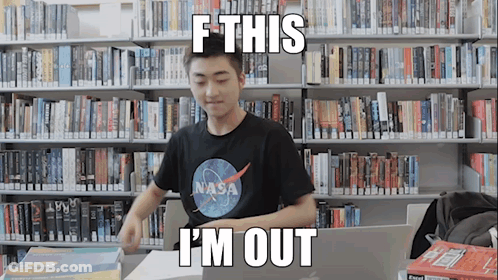 A Man Wearing A Nasa Shirt Is Sitting At A Desk In A Library GIF
