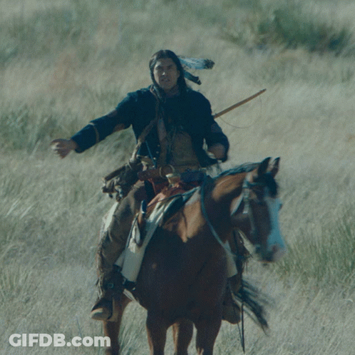A Man Wearing A Native American Headdress Rides A Brown Horse GIF