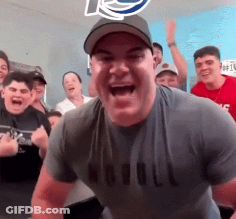A Man Wearing A Naval Shirt Is Laughing In Front Of A Crowd Of People GIF
