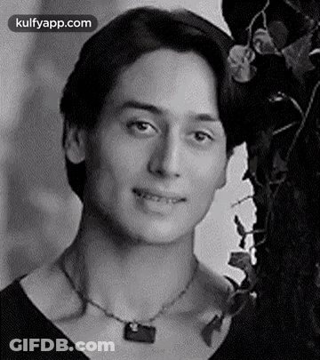 A Man Wearing A Necklace Is Smiling In A Black And White Photo . GIF