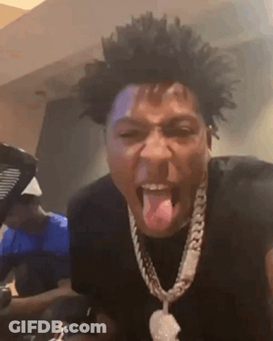 A Man Wearing A Necklace Is Sticking His Tongue Out While Making A Funny Face . GIF