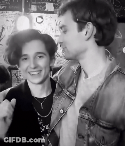 A Man Wearing A Necklace That Says ' The Singer ' On It Stands Next To Another Man GIF