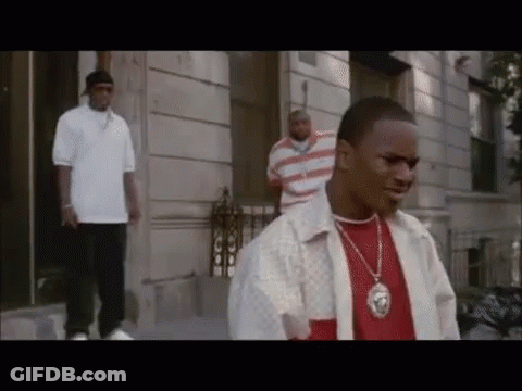A Man Wearing A Necklace With A Lion On It Is Standing In Front Of A Building GIF