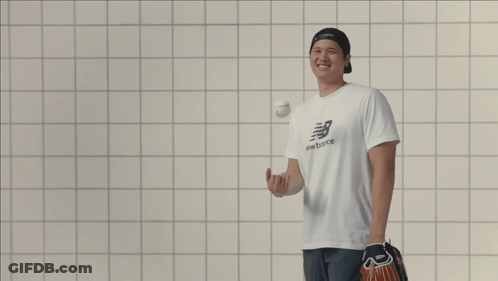 A Man Wearing A New Balance T-Shirt Laughs While Holding A Baseball GIF