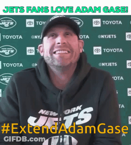 A Man Wearing A New York Jets Hoodie Smiles In Front Of A Green Backdrop GIF