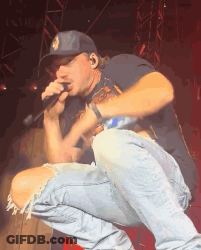 A Man Wearing A New York Yankees Hat Is Singing Into A Microphone On A Stage GIF