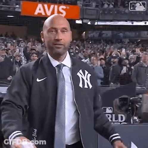 A Man Wearing A New York Yankees Jacket And Tie Is Throwing A Baseball In Front Of A Crowd . GIF