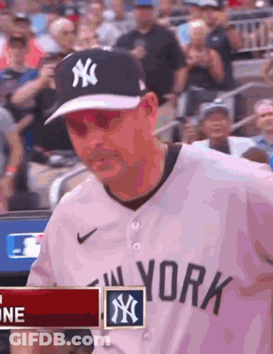A Man Wearing A New York Yankees Jersey Is Standing In Front Of A Crowd GIF