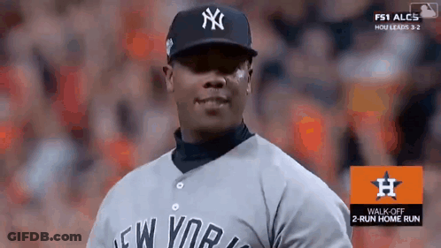 A Man Wearing A New York Yankees Jersey Stands In Front Of A Sign That Says Walk Off 2 Run Home Run GIF