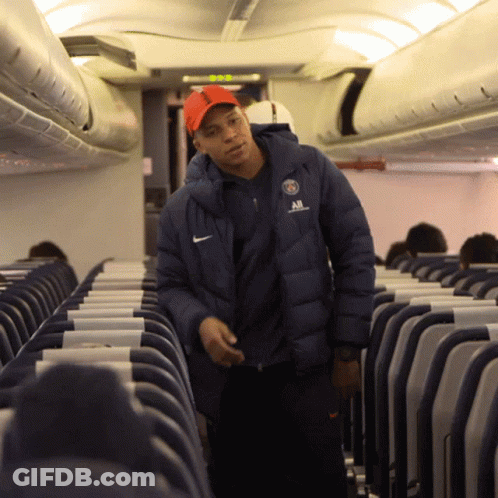 A Man Wearing A Nike Jacket Stands In An Airplane Aisle GIF