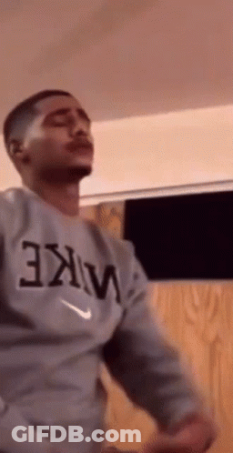 A Man Wearing A Nike Shirt Is Dancing In A Room . GIF