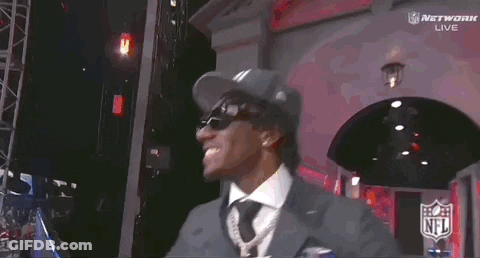 A Man Wearing A Ny Hat And Sunglasses Stands In Front Of A Screen GIF