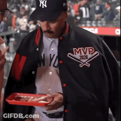 A Man Wearing A Ny Yankees Baseball Jacket Holds A Tray Of Food GIF