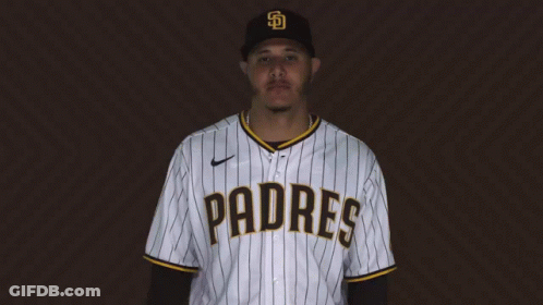 A Man Wearing A Padres Baseball Jersey Stands In Front Of A Brown Background GIF