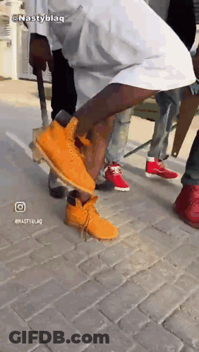 A Man Wearing A Pair Of Orange Timberland Boots Is Standing On A Brick Sidewalk GIF