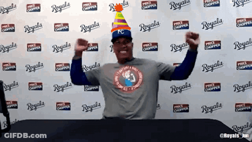 A Man Wearing A Party Hat Is Standing In Front Of A Wall That Says Royals On It GIF