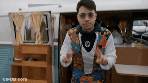 A Man Wearing A Peace Sign Necklace Is Dancing In Front Of A Van GIF