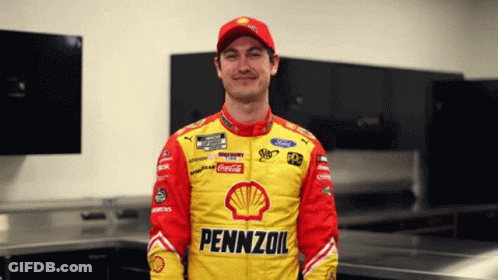 A Man Wearing A Pennzoil Jacket Stands In A Room GIF