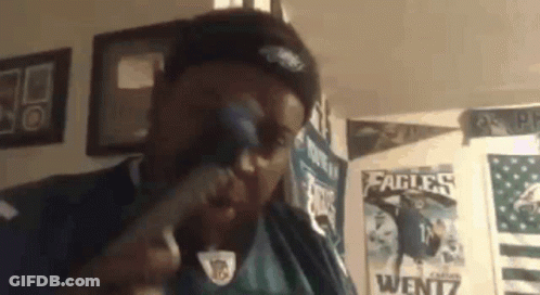 A Man Wearing A Philadelphia Eagles Jersey Is Singing Into A Microphone In A Room . GIF