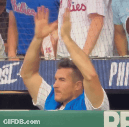 A Man Wearing A Phillies Jersey Holds His Arms Up In The Air GIF
