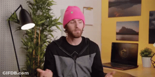 A Man Wearing A Pink Beanie Is Sitting In Front Of A Laptop Computer GIF