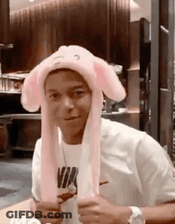 A Man Wearing A Pink Bunny Hat Is Sitting At A Table In A Restaurant . GIF