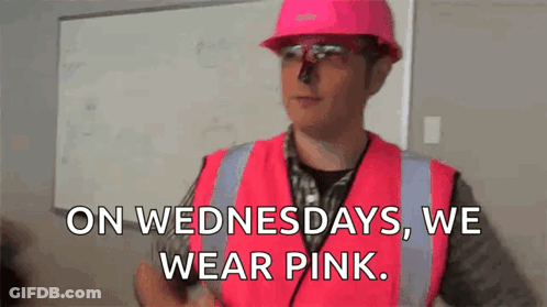 A Man Wearing A Pink Hard Hat And Safety Vest Is Standing In Front Of A Whiteboard . GIF
